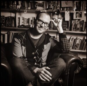 Cory Doctorow sitting on a large chair in front of a bookshelf